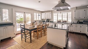 Een ruime keuken met witte kastjes, een groot kookeiland en een eetgedeelte met houten stoelen.