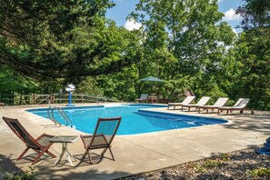 Une piscine entourée d’arbres, avec des chaises longues et une table à proximité.