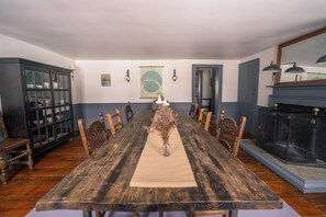 Une longue table de salle à manger en bois, ornée d’un vase de fleurs séchées au centre, et entourée de chaises.