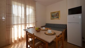 A small, well-lit room with a dining table set for two, a sofa, a refrigerator, and a painting on the wall. - Comfort and style in Bibione - Beahost (Bibione)
