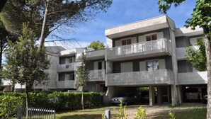 A multi-story residential building with balconies, a parking area, and a gated entrance. - Comfort and style in Bibione - Beahost (Bibione)