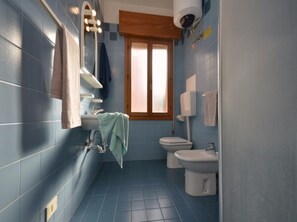 A bathroom with blue tiles, a bathtub, a sink, a toilet, and a bidet.