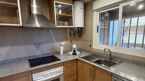 A modern kitchen with a built-in stove, oven, and dishwasher, wooden cabinets, and a window with a view. - CB250 - Cala Blanca II, Superior - ServHouse (Orpesa)