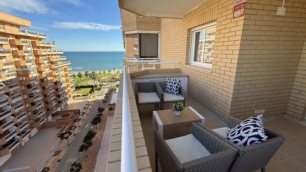 A balcony with wicker furniture, a TV, and a view of the ocean. - CB250 - Cala Blanca II, Superior - ServHouse (Orpesa)