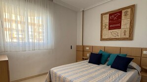 A bedroom with a bed, a ceiling fan, a window with sheer curtains, and a wall-mounted artwork. - CB250 - Cala Blanca II, Superior - ServHouse (Orpesa)