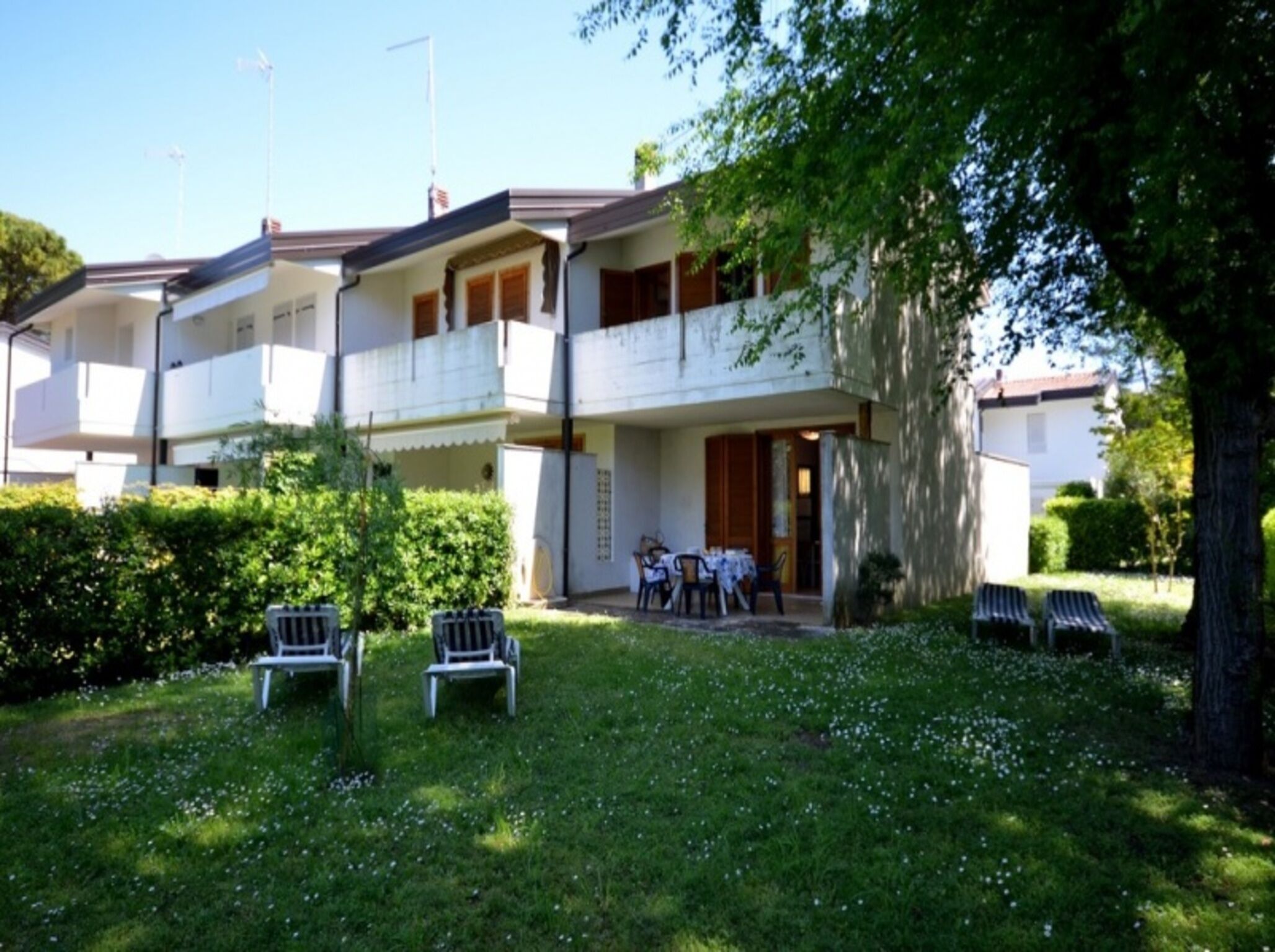 A two-story building with a balcony, a small garden with chairs, and a tree.