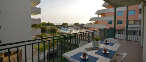 A balcony with a table set for two, overlooking a swimming pool and adjacent buildings.