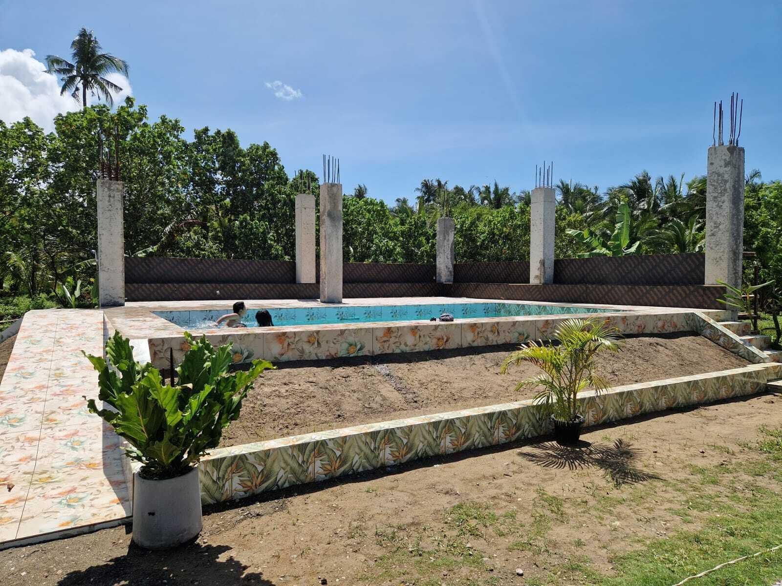 A swimming pool with a tiled deck, surrounded by concrete pillars and a fence.