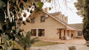 A two-story house with a brick exterior, a covered patio with outdoor furniture, and a large window with a view of the garden.