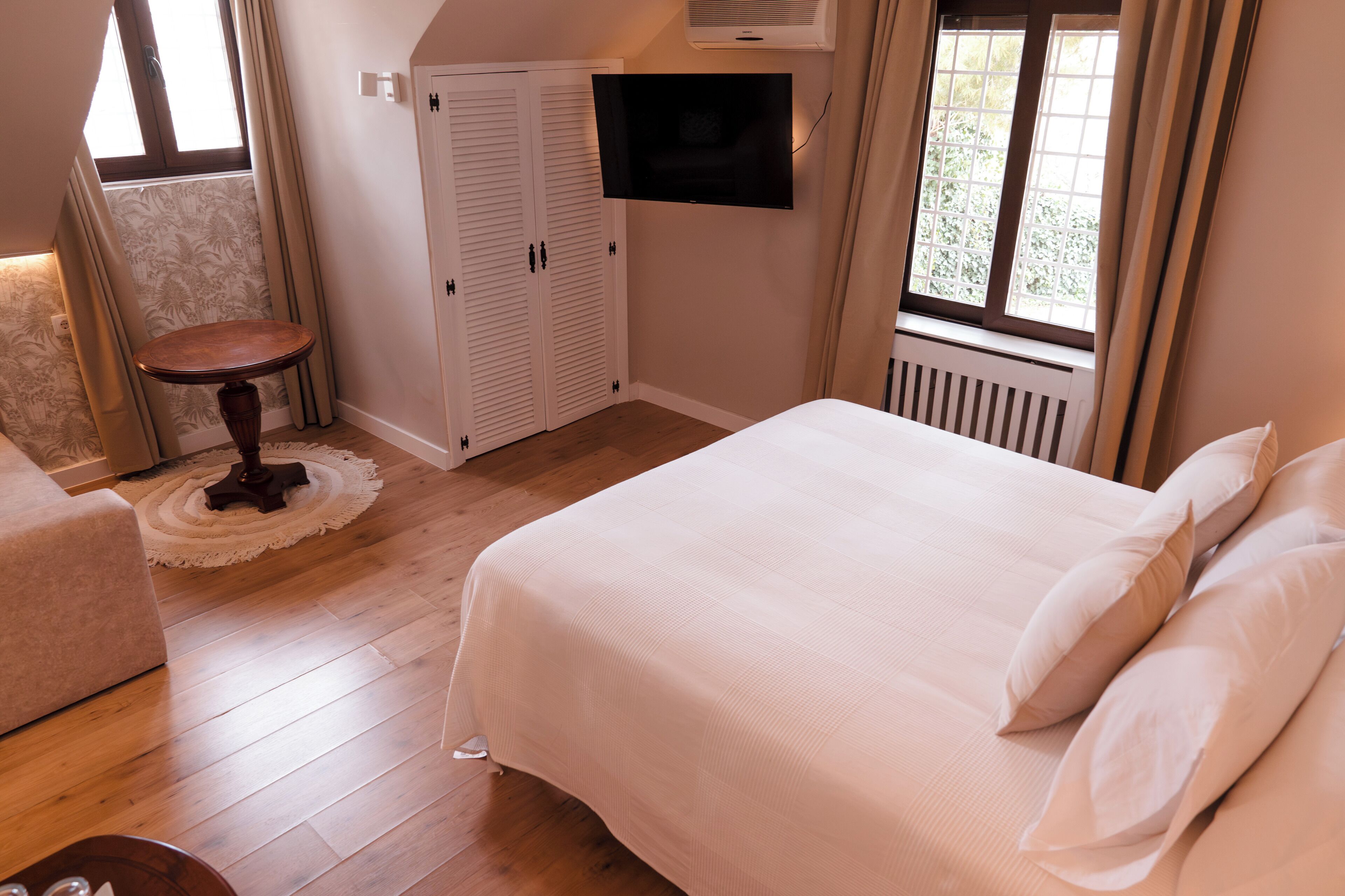 Un dormitorio con cama, televisor montado en la pared, armario y una mesita.