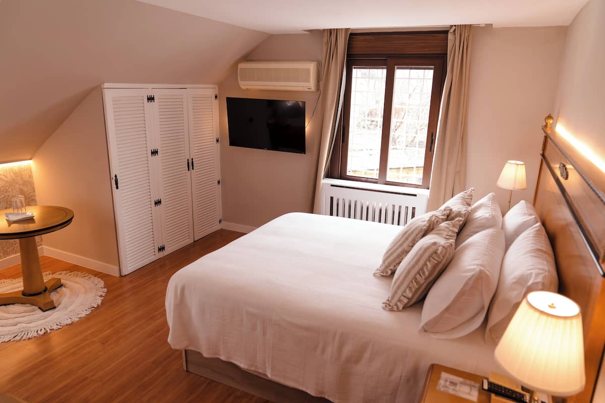 A bedroom with a bed, bedside lamps, a TV, a wardrobe, and a window with curtains.