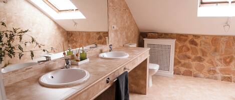 A bathroom with two sinks, a mirror, a towel rack, and a stone wall.