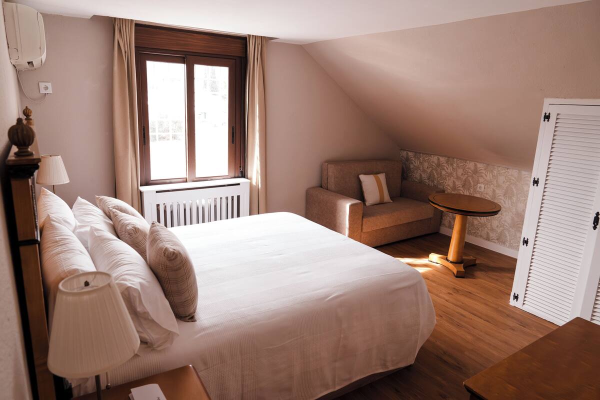 A bedroom with a large bed, a sofa, a small table, and a radiator.