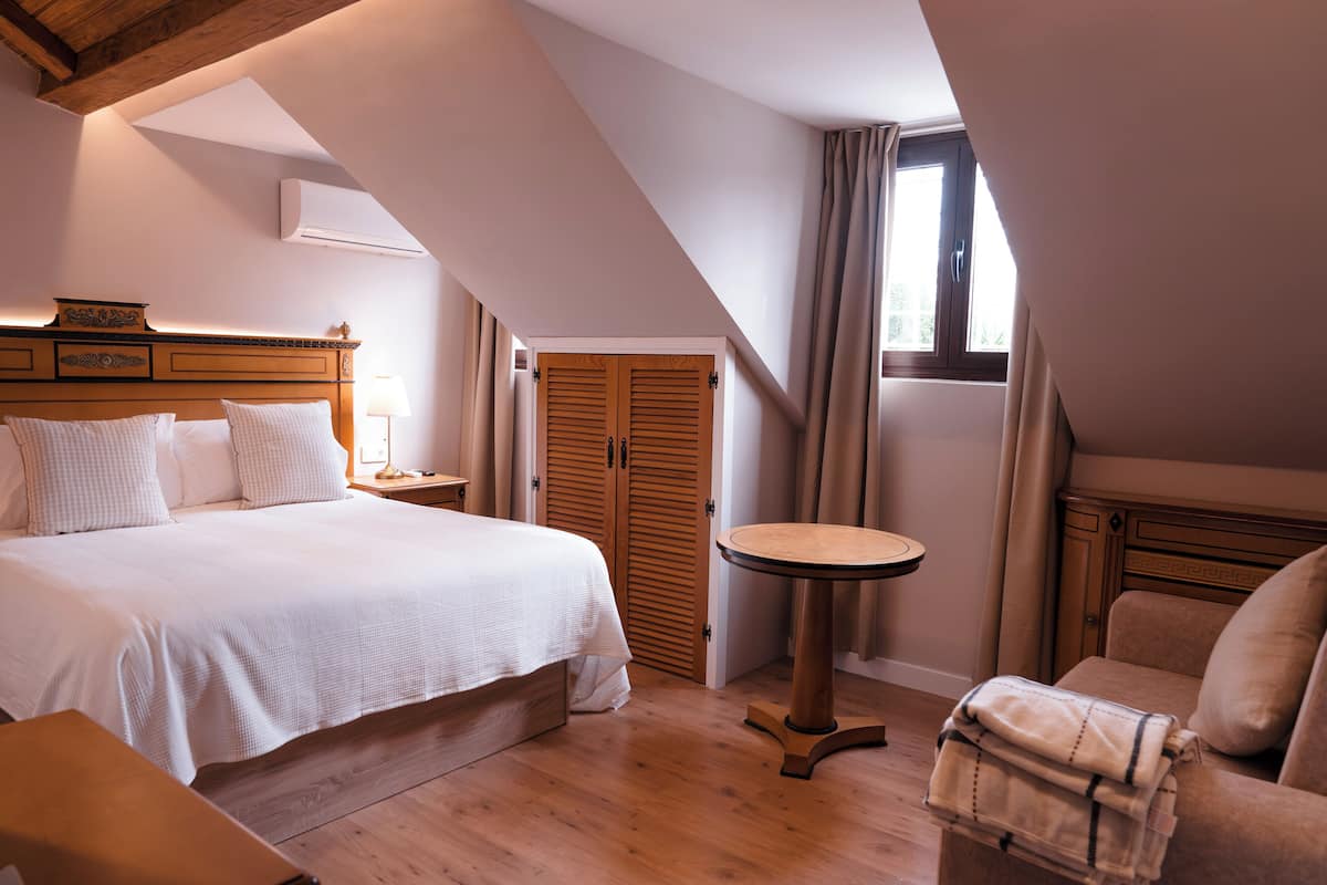 A bedroom with a large bed, a wooden nightstand, a round table, a chair, and a wardrobe.