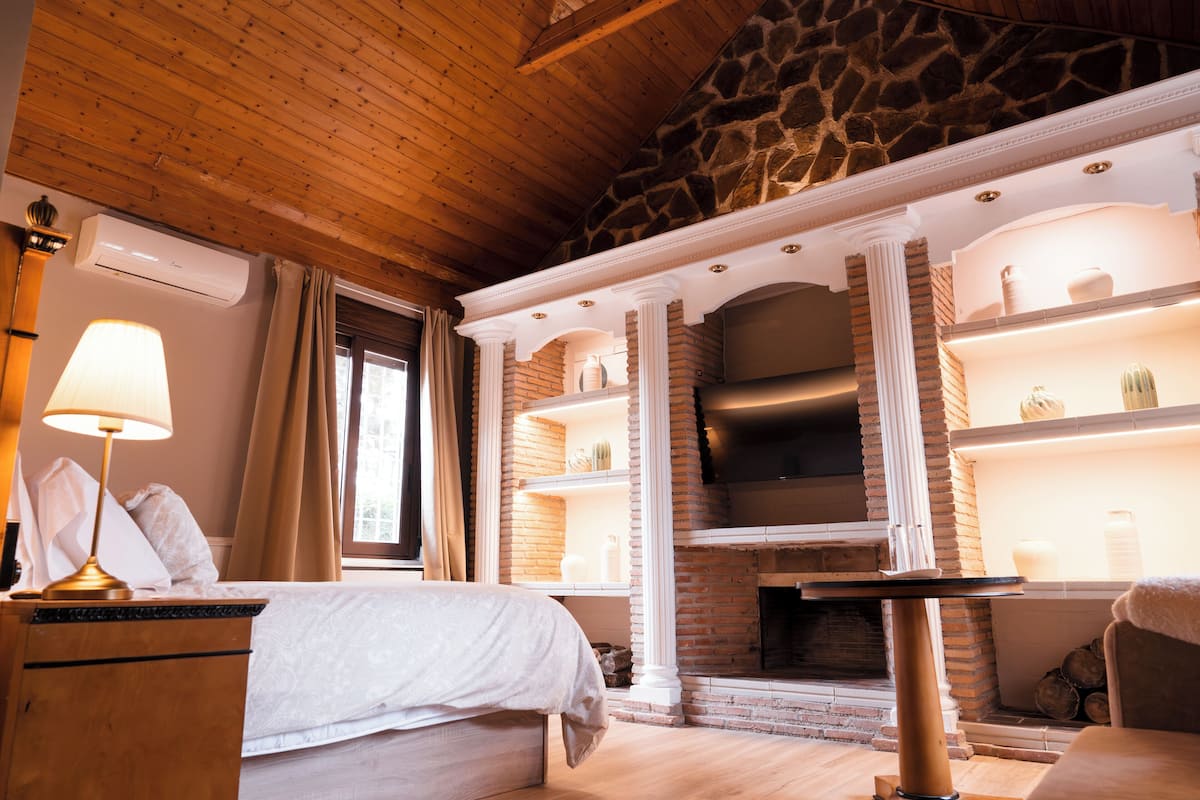 A room with a bed, a fireplace, and a stone wall.