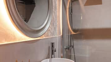 A bathroom with a round mirror, a sink, and a glass-enclosed shower.