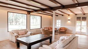 A spacious living room with wooden beams, large windows, and a fireplace.