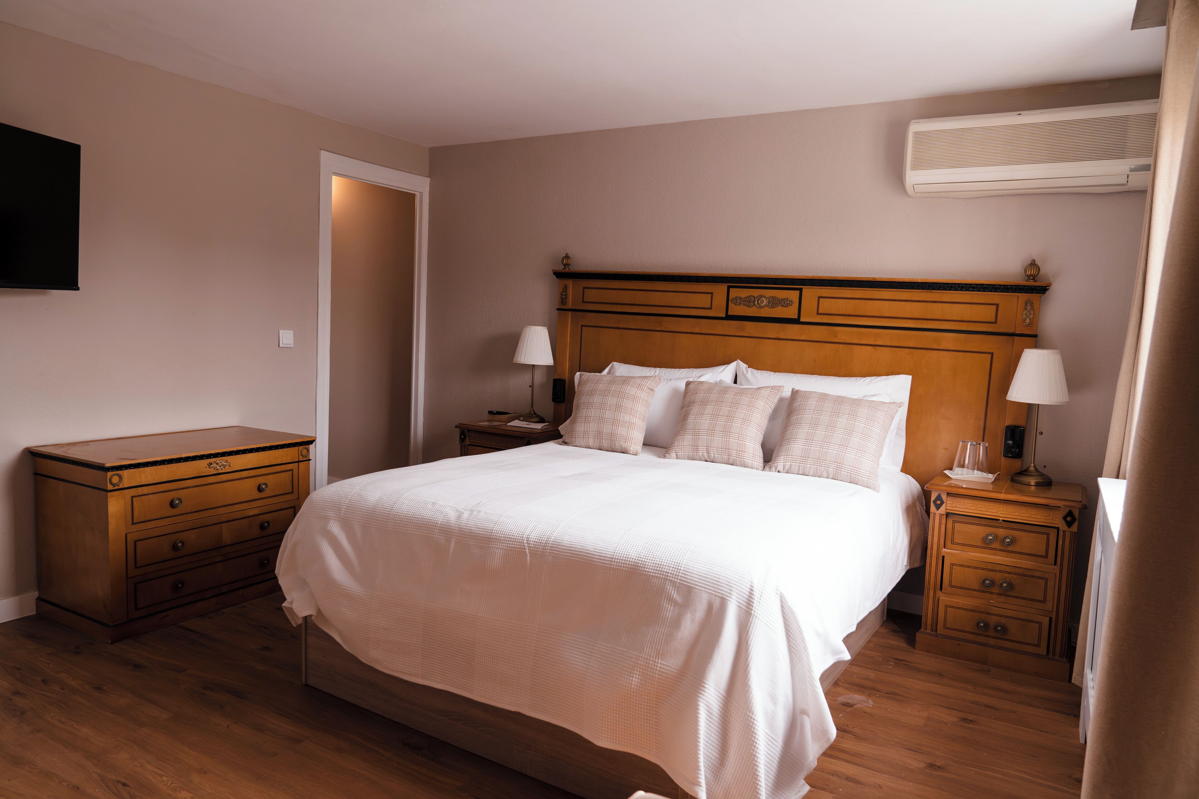 A neatly arranged bedroom with a large bed, wooden nightstands, and a flat-screen TV on the wall.