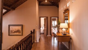 A hallway with wooden beams, a framed picture on the wall, a bedside table with a lamp, and a mirror.