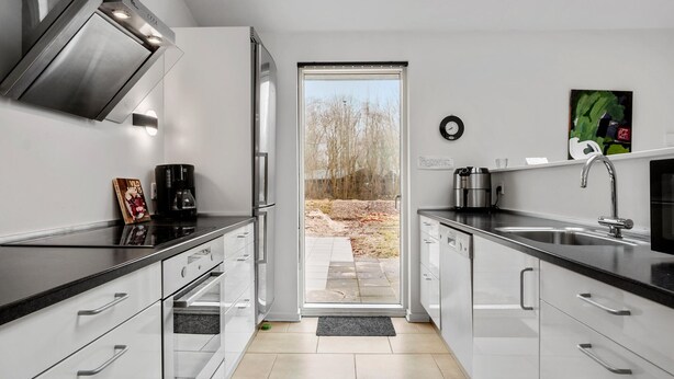 A modern kitchen with white cabinets, black countertops, stainless steel appliances, and a view through the door to an outdoor area.