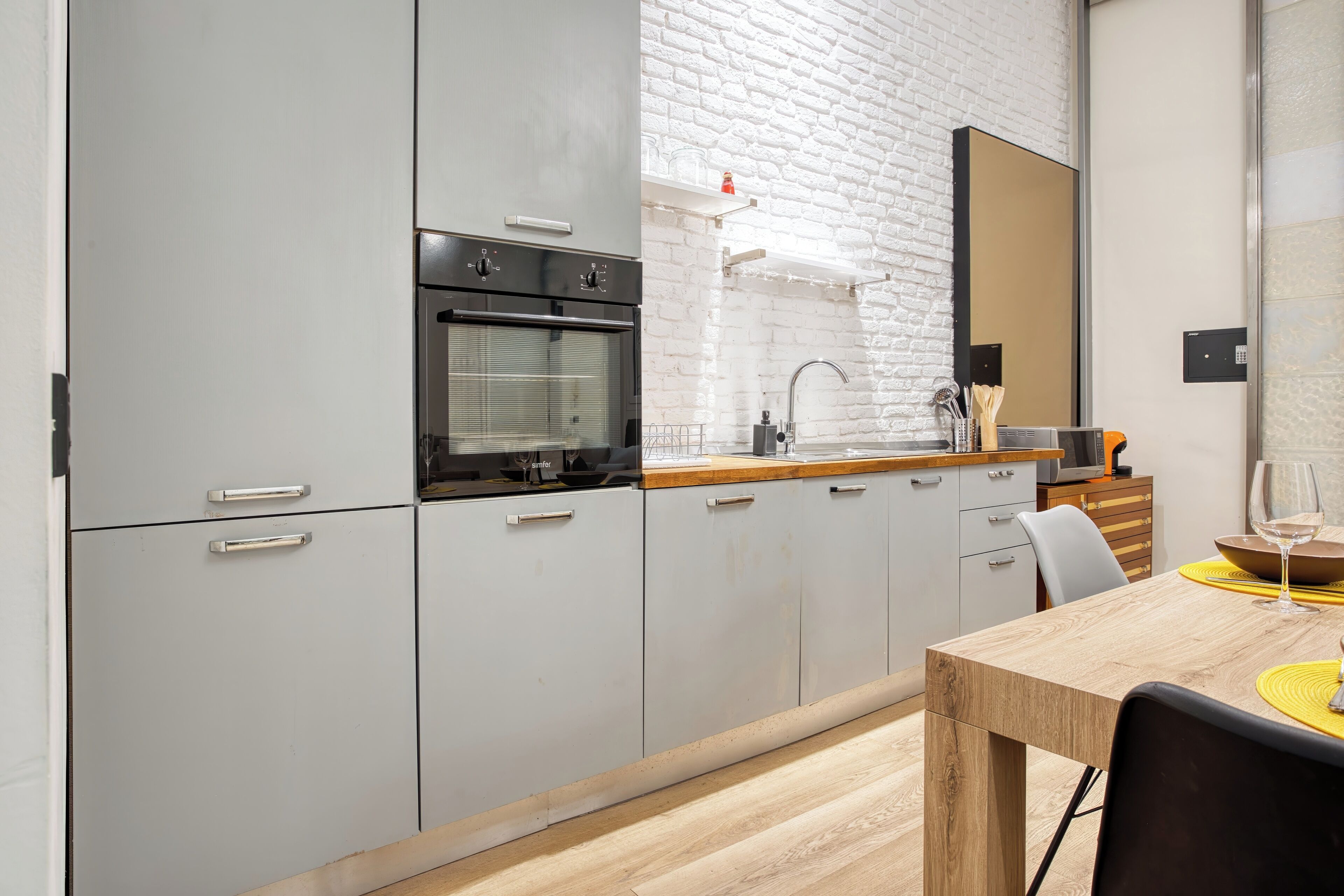 Une cuisine moderne avec des meubles gris, un plan de travail en bois et un coin repas comprenant une table et des chaises.