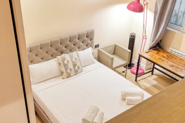 A neatly made bed with a tufted headboard, a bedside table with a lamp, and a chair.