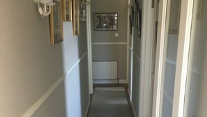 Un couloir étroit doté d’un sol recouvert de moquette, de boiseries blanches et d’un radiateur fixé au mur.