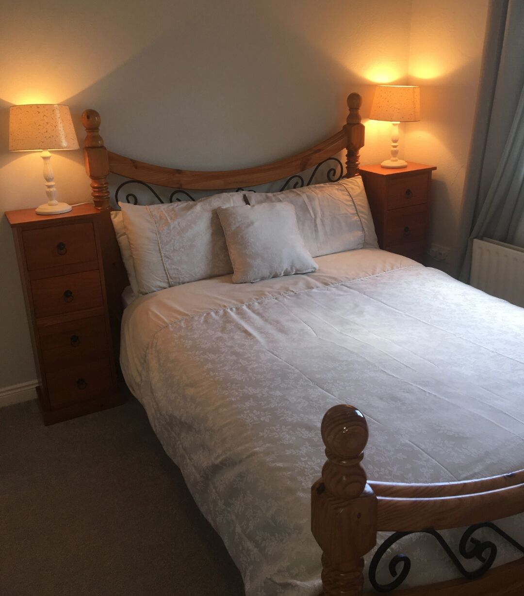 A bedroom with a wooden bed frame, two bedside tables with lamps, and a radiator.
