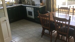 Une cuisine avec des meubles de rangement de couleur sombre, une cuisinière et une table à manger avec des chaises.