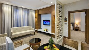 Una habitación de hotel moderna con sofá, televisor montado en la pared, una mesita con fruta y un separador decorativo.