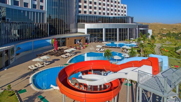 Un resort con un amplio área de piscina, tobogán de agua y numerosas tumbonas.