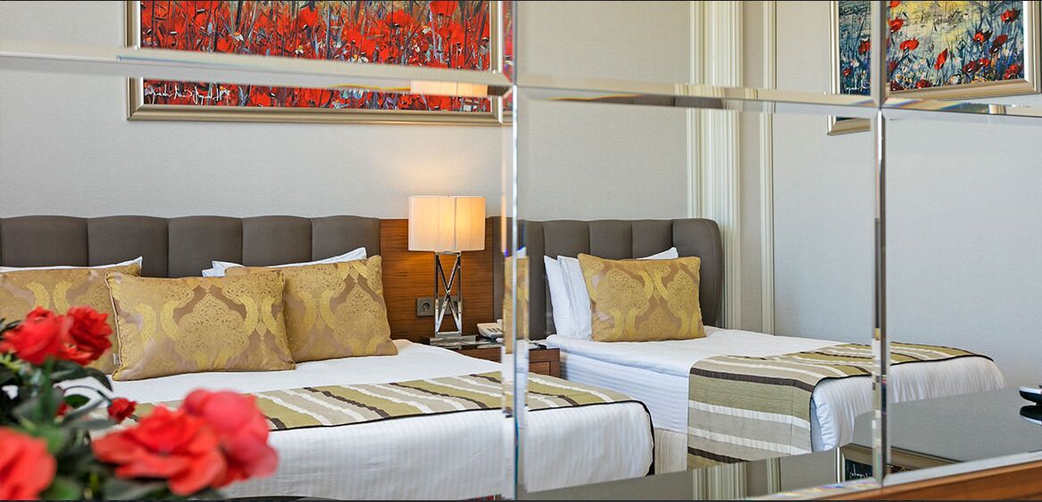 Een hotelkamer met twee bedden, een nachtkastje, een lamp en kunst aan de muren.