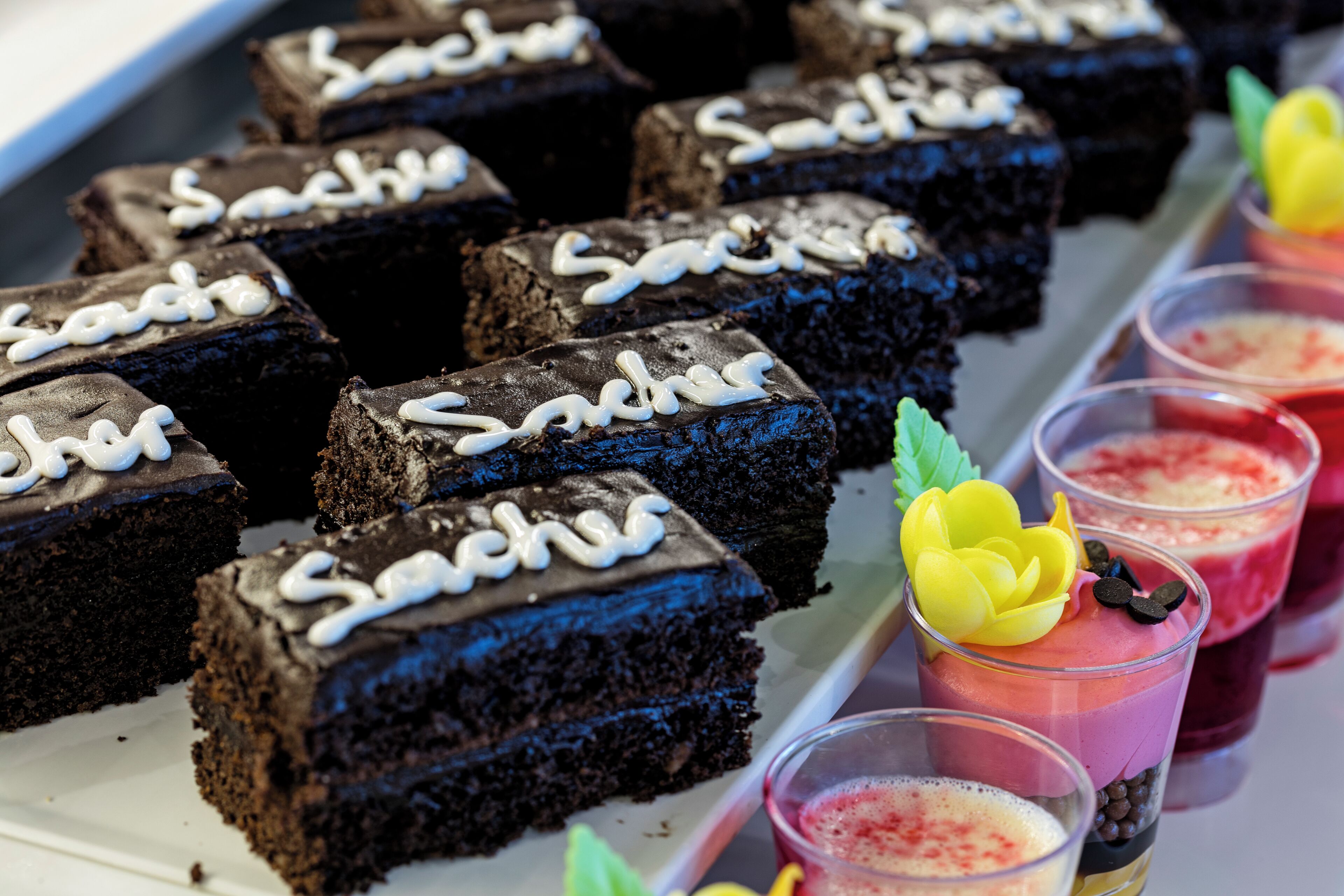 A tray of chocolate brownies with white icing and a yellow flower decoration.
