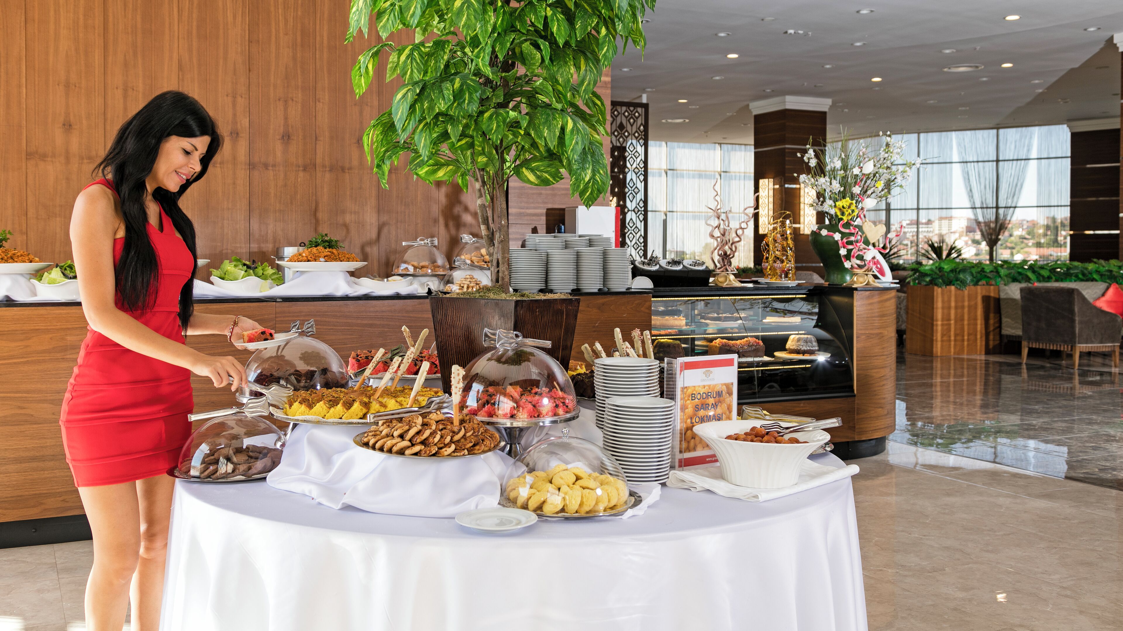 Disposição de buffet com diversos alimentos e uma mulher servindo.
