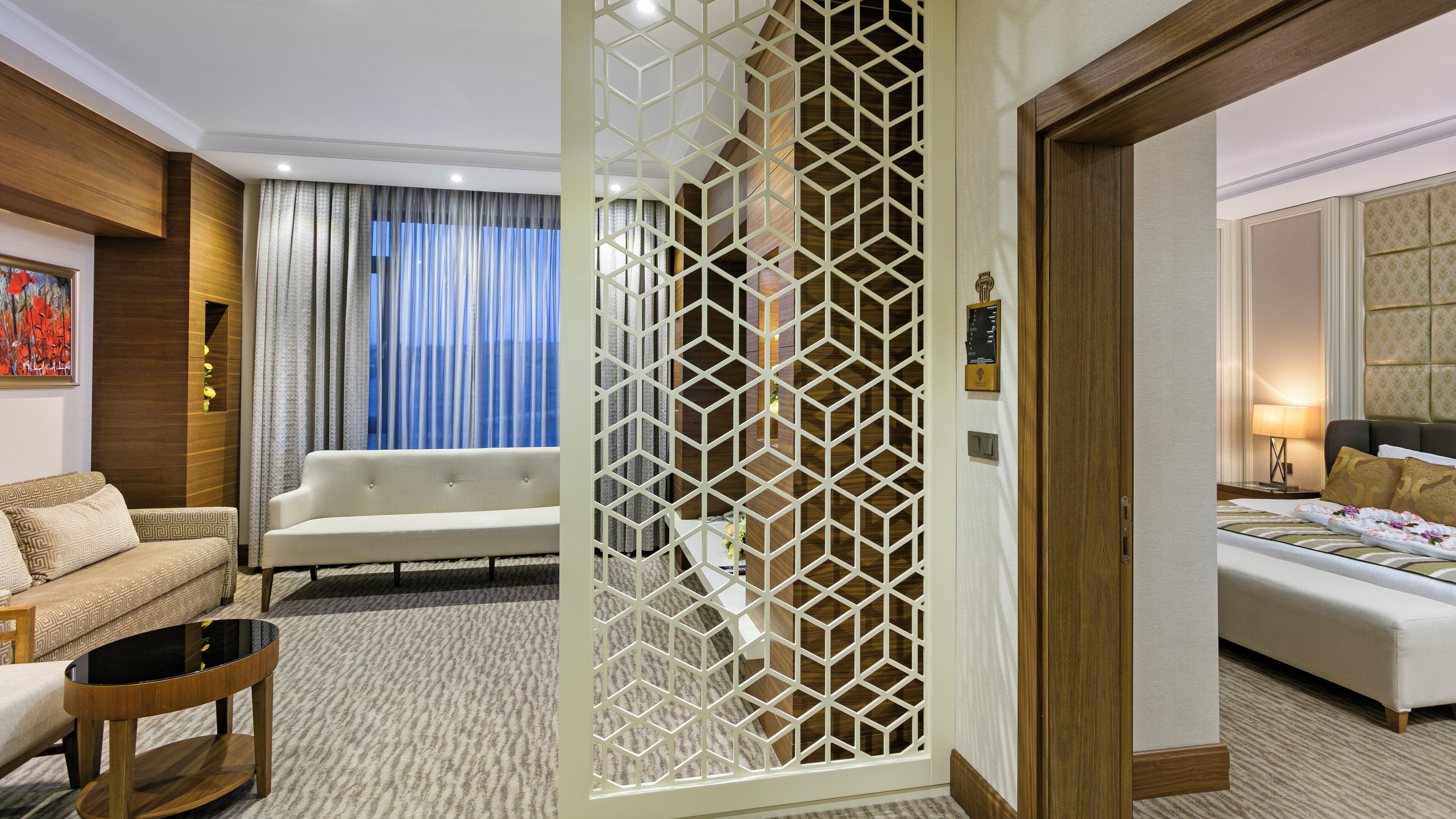 A hotel room with a sofa, a coffee table, a bed, and a decorative partition.