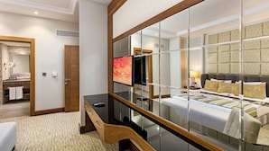 Habitación de hotel con un espejo grande, televisor, cama, escritorio y baño.