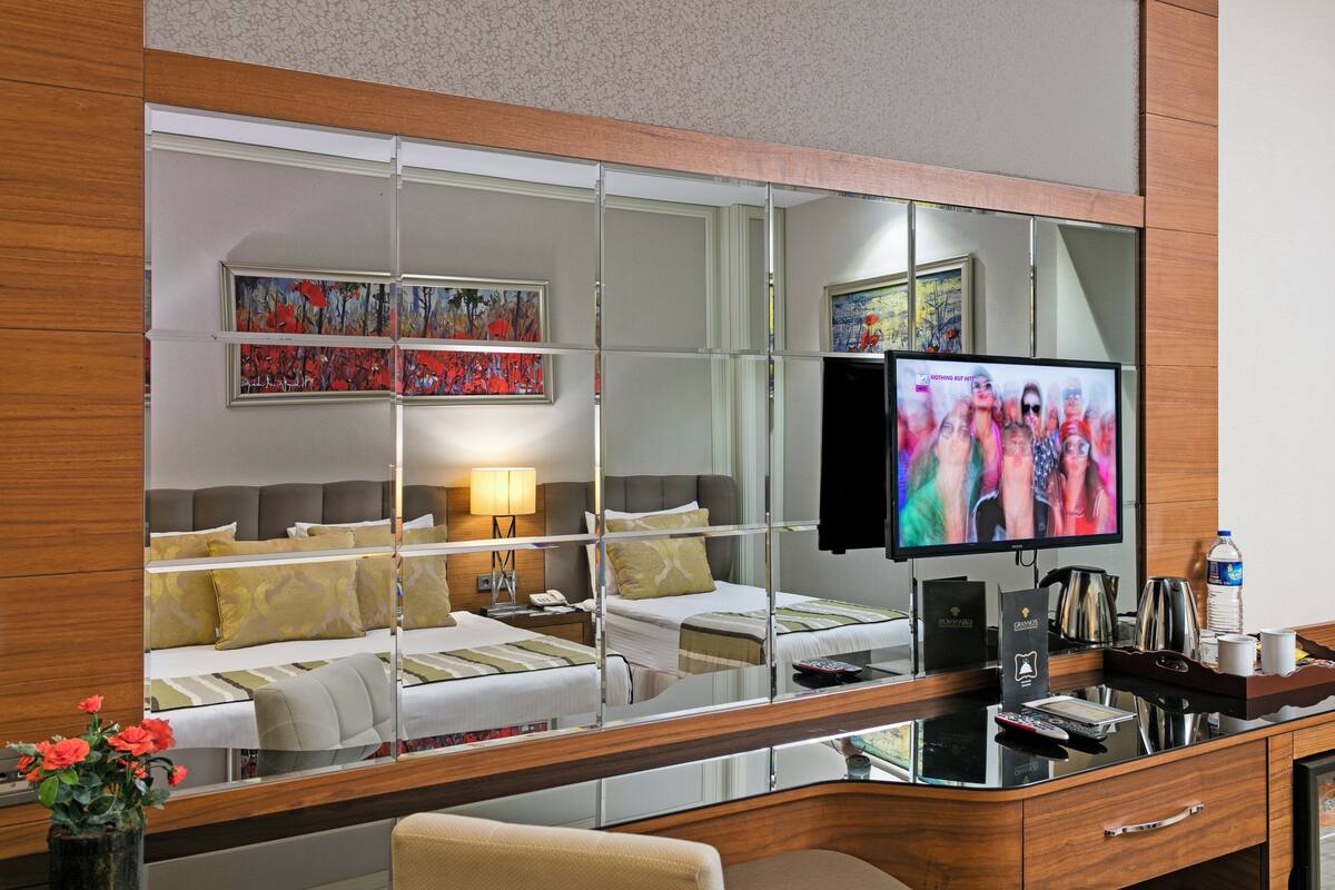 Habitación de hotel con un espejo grande que refleja la cama, un televisor y una obra de arte en la pared.