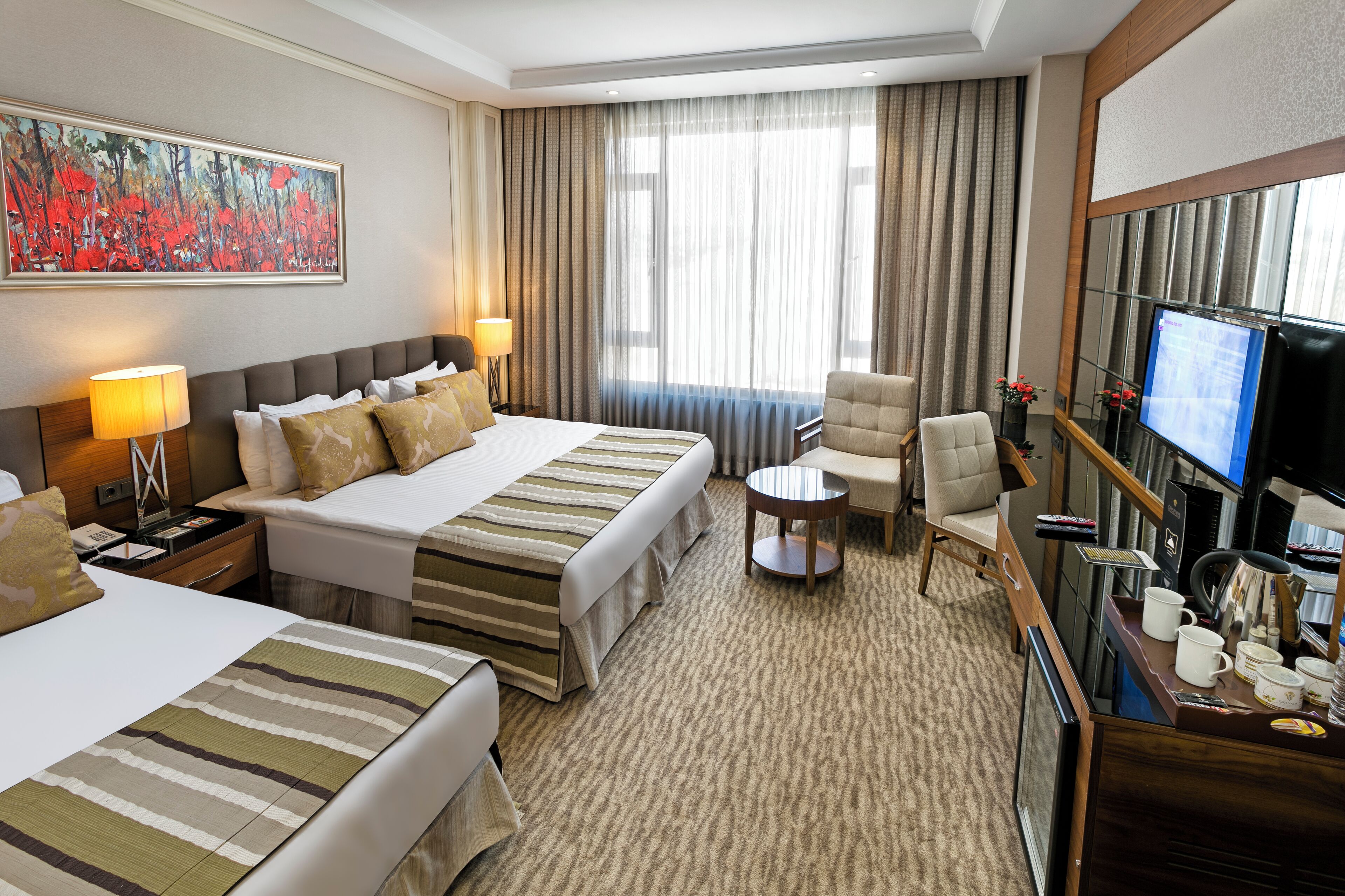 A hotel room with two beds, a desk, a chair, a TV, and a large window with curtains.