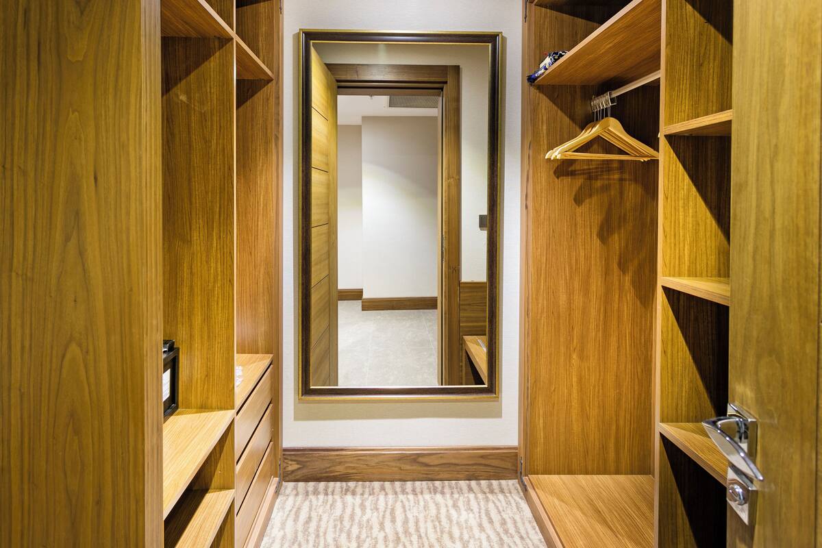 Un vestidor con estantes de madera y puerta con espejo.