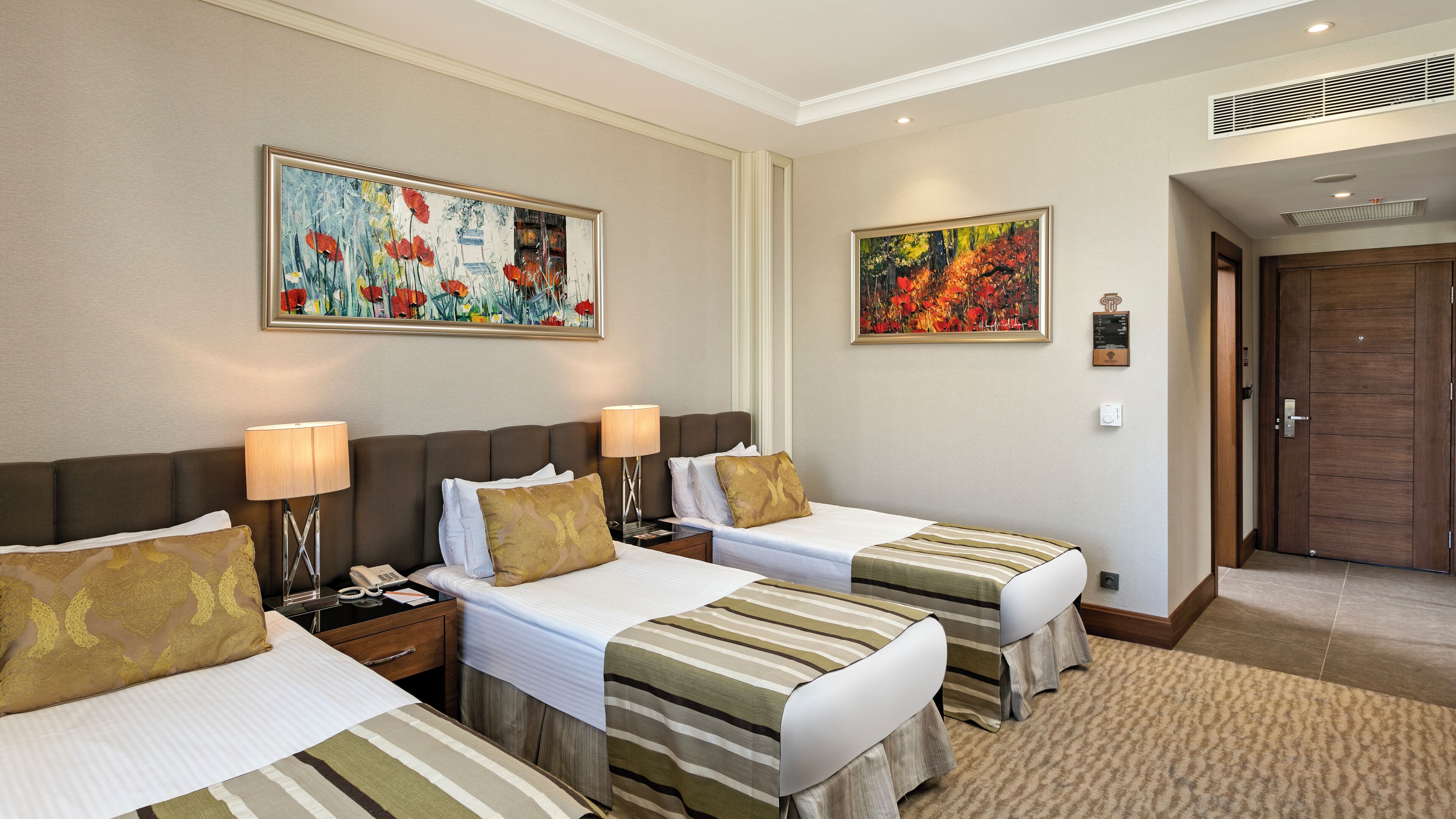 A hotel room with two beds, each with a striped bedspread, a nightstand with a lamp, and a painting above the beds.