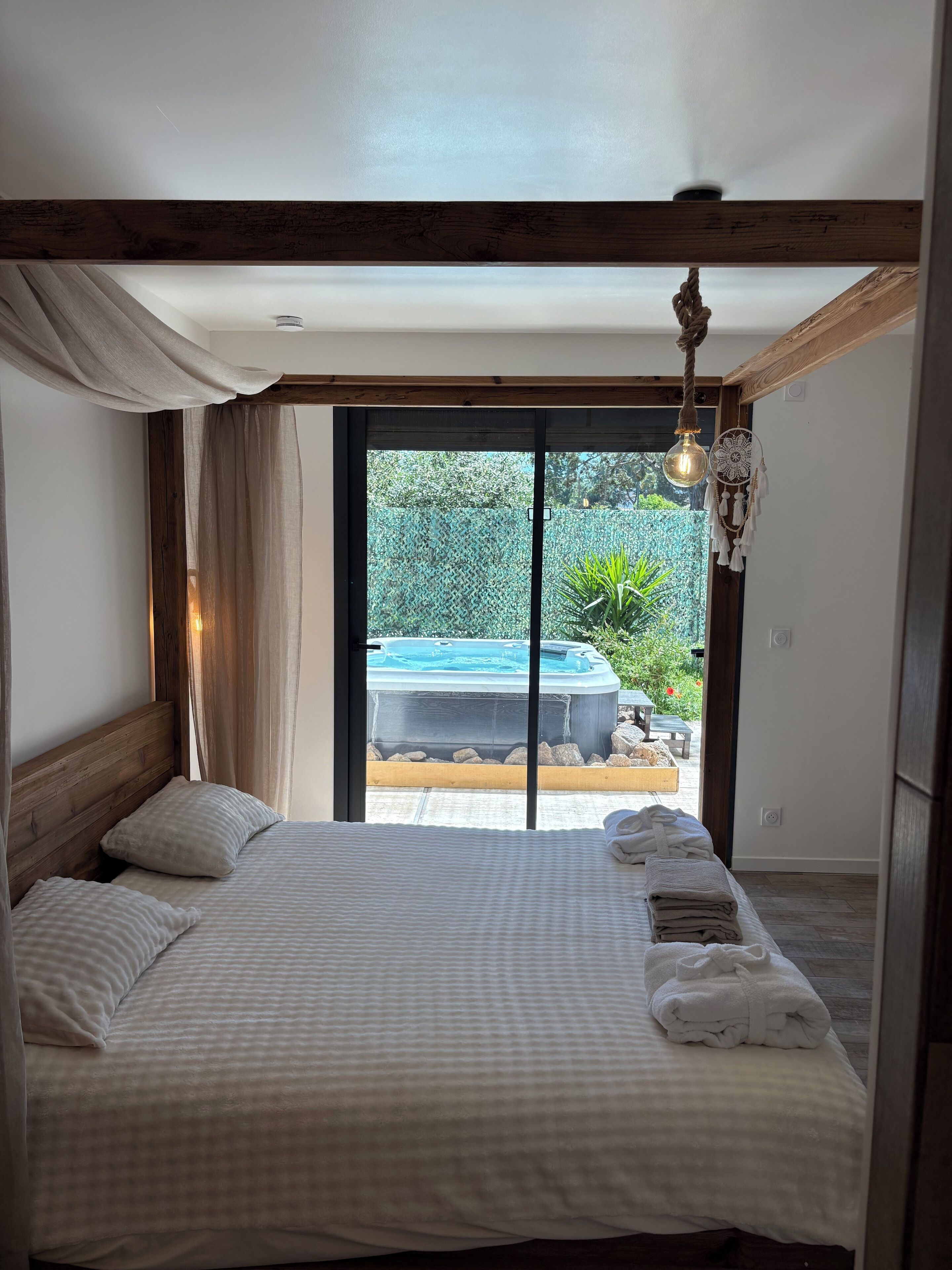 Ein Schlafzimmer mit Bett, einer Pendelleuchte und Blick auf ein Außen-Whirlpool und eine Terrassenanlage.
