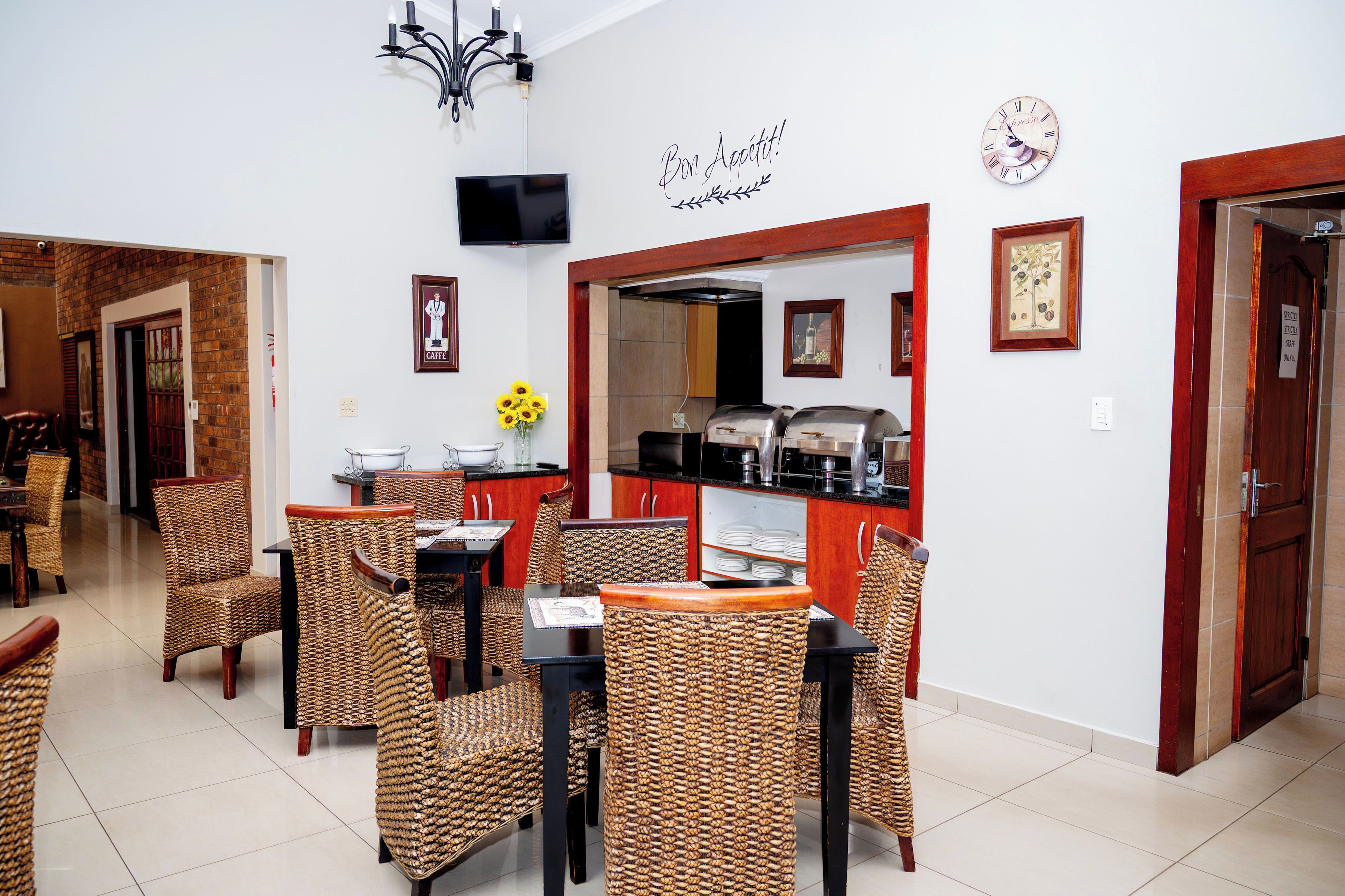 A dining area with wicker chairs and tables, a kitchen with a coffee machine, and a clock on the wall.