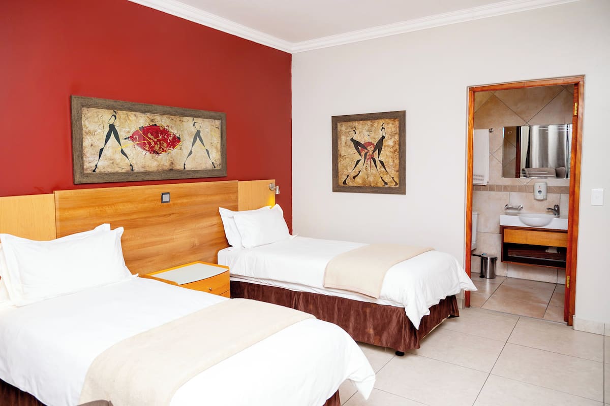 A hotel room with two beds, a wooden headboard, a red accent wall, and artwork above the beds.