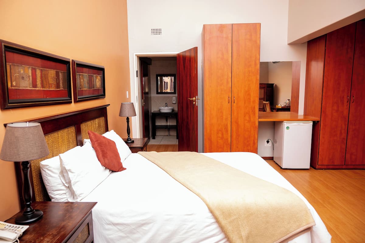 A hotel room with a bed, a nightstand, a lamp, a wardrobe, and a small kitchenette.