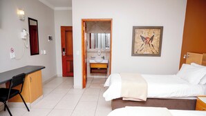 A hotel room with a desk, two beds, a bathroom with a sink, and a shower.