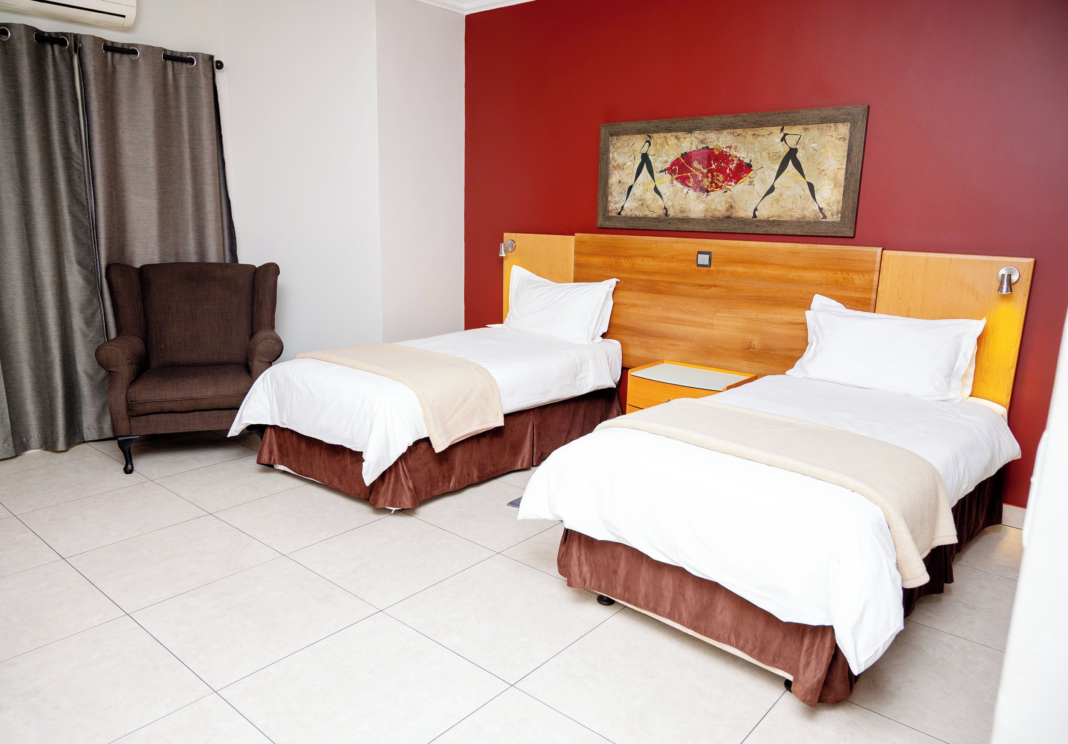 A hotel room with two beds, a chair, and a painting on the wall.