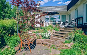 A garden with a wooden bench, stone steps, and a building with a porch.