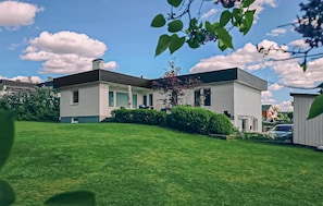 Een modern huis met twee verdiepingen, een verzorgd gazon, een kleine boom en een auto op de oprit.