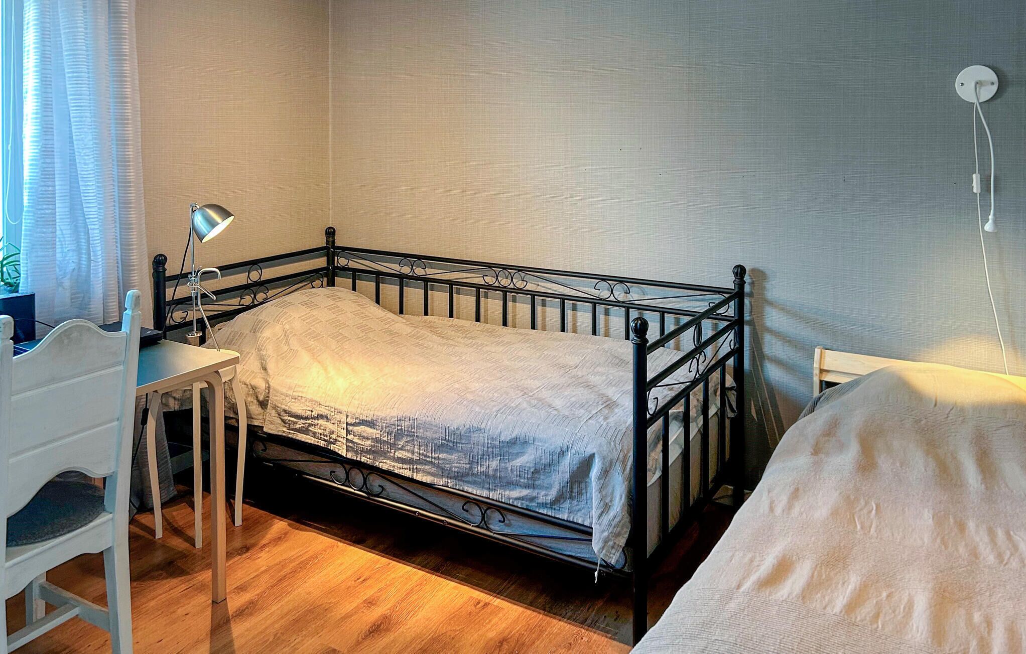 Un lit simple avec un cadre en métal, une table de chevet avec une lampe et une chaise.