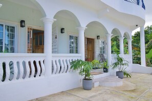 A covered outdoor area with white columns, potted plants, and a tiled floor.